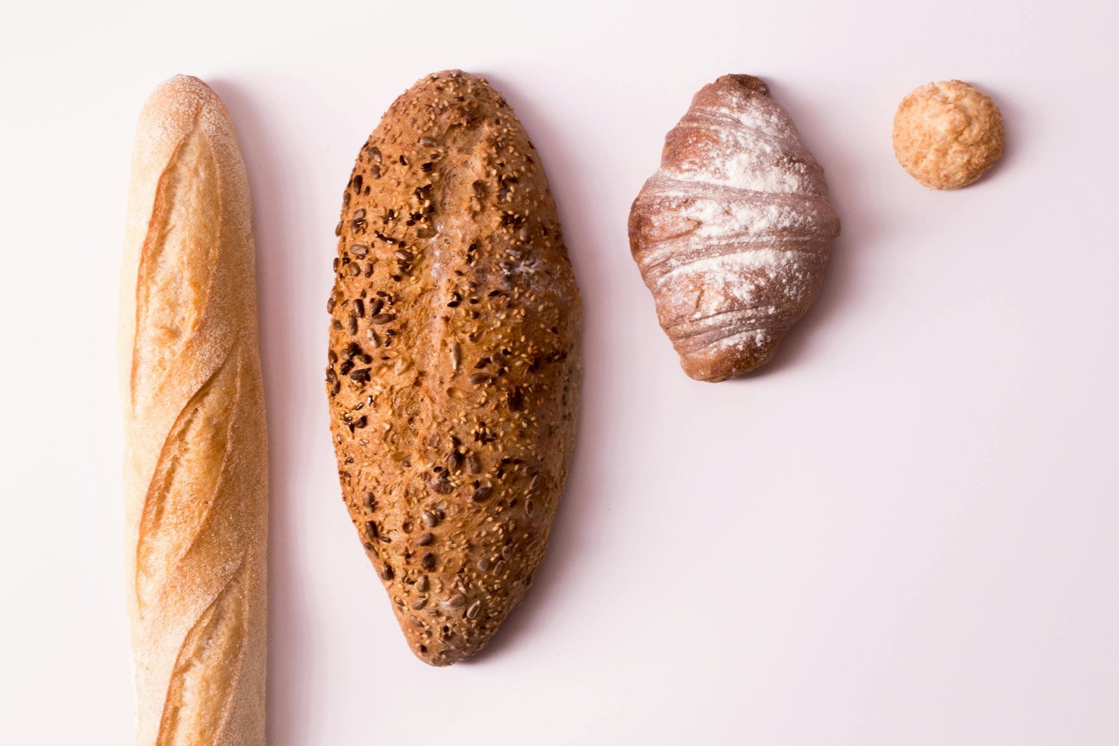 Variety of breads including a croissant, baguette, and seeded loaf on a clean white surface.