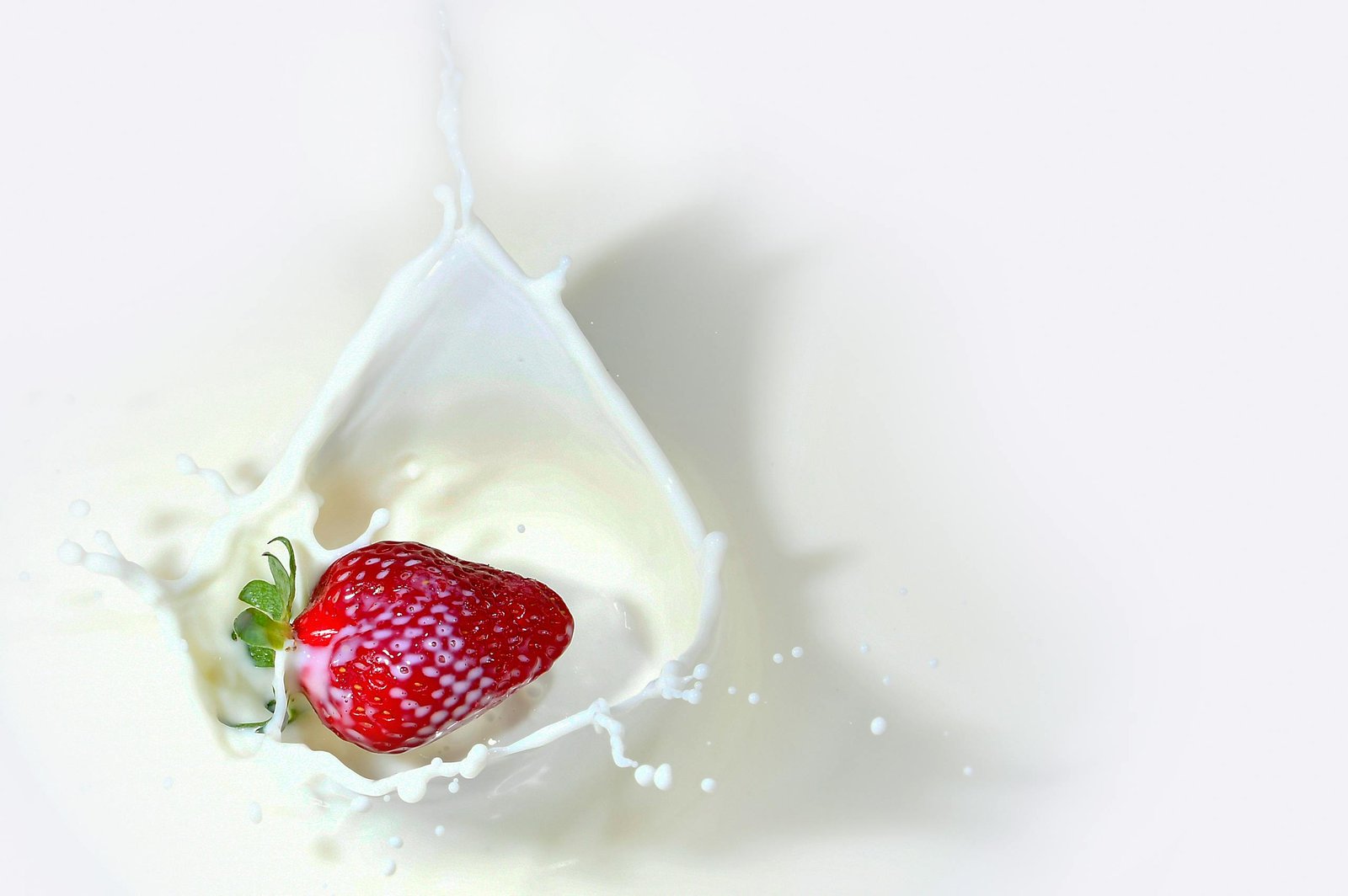 Vibrant strawberry captured splashing into milk, creating dynamic movement and texture.